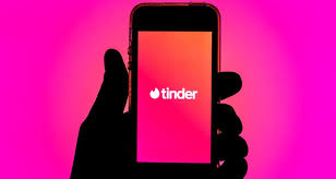 "Logo de Tinder en la pantalla de un smartphone con un fondo rosa."