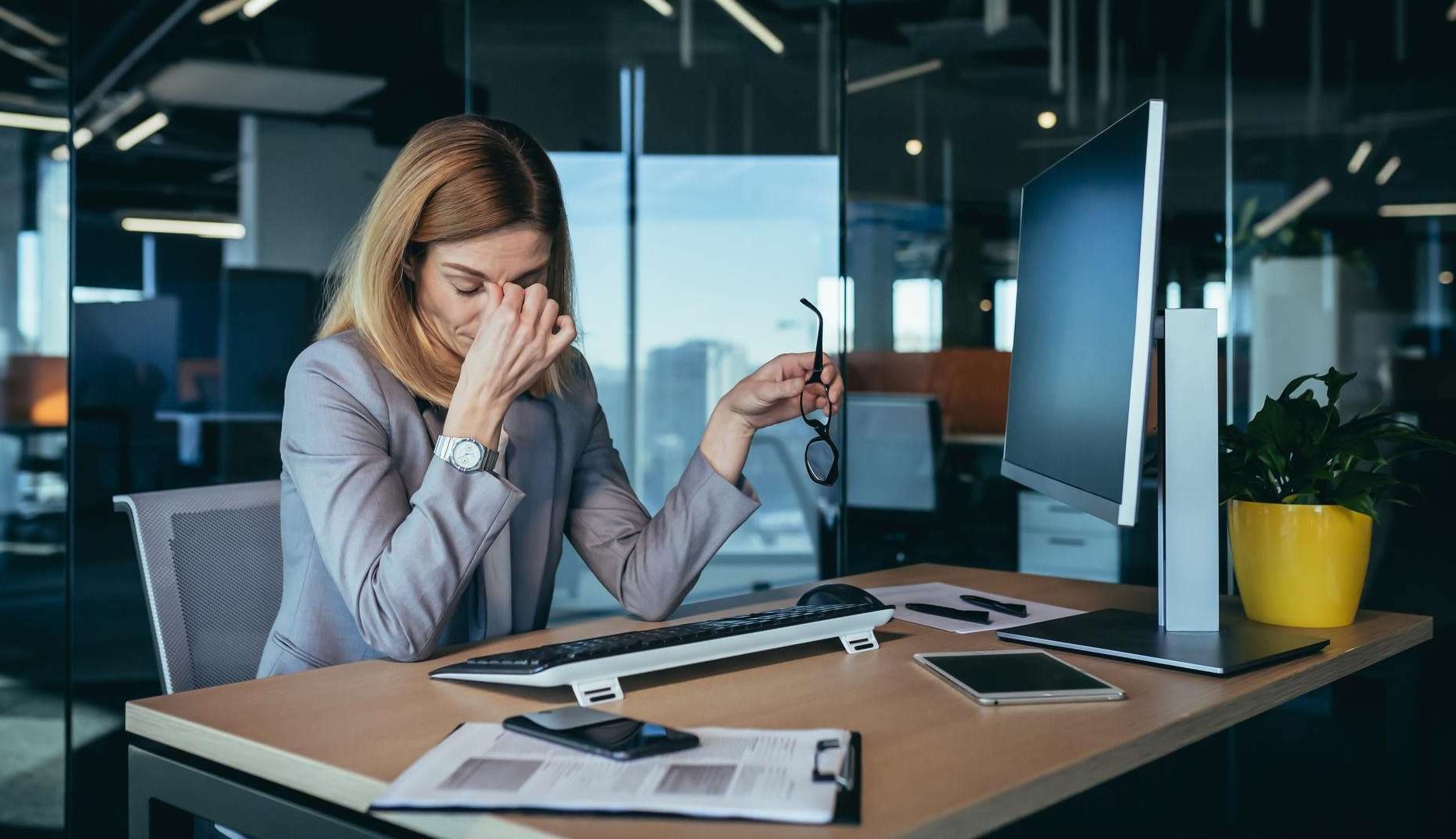 Mujer en la oficina mostrando signos de estrés mientras se quita las gafas